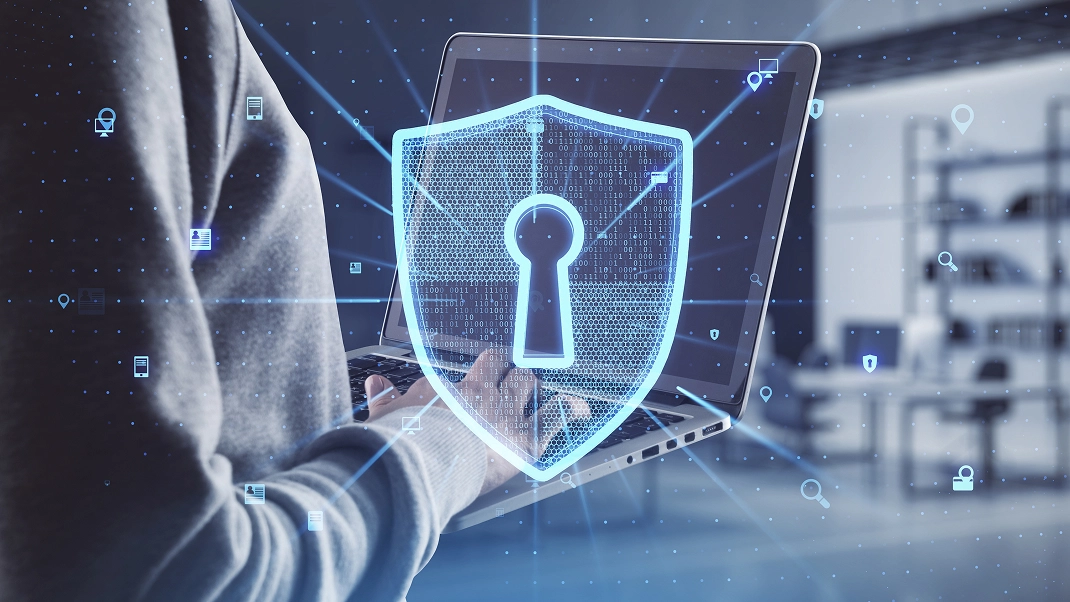 Person using a laptop with digital security shield overlay, symbolizing cybersecurity and data protection.
