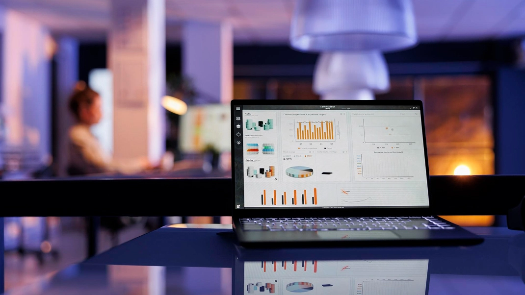 Laptop displaying data analytics charts in a dimly lit office setting, highlighting business insights and technology.