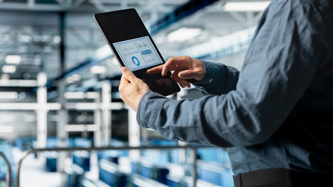 Person using tablet with analytics dashboard in a modern warehouse setting.
