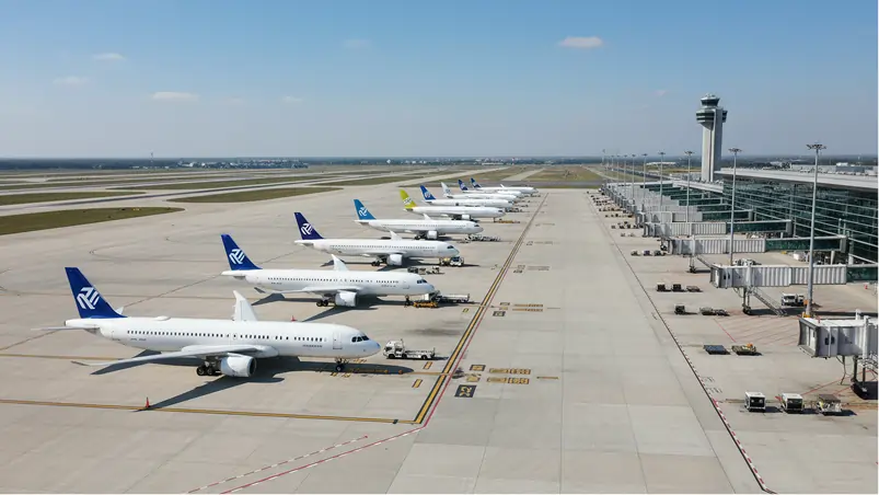 Airplanes parked at a busy airport terminal, with a control tower in the background under a clear blue sky.