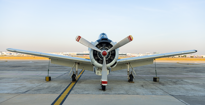 Vintage propeller aircraft on airport runway, viewed from behind, under a clear sky.