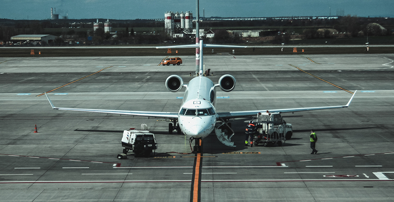 Airplane on runway being serviced with ground crew at airport, clear sky background.