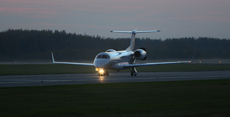 Private jet lands on runway at dusk with forest backdrop, highlighting luxury air travel and evening ambiance.